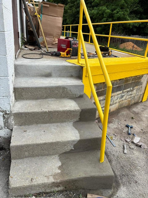 Concrete steps and new yellow handrail beside loading dock