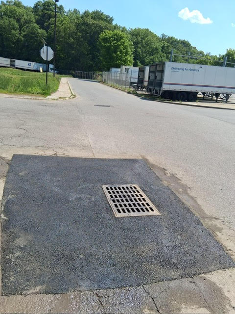 Repaired storm drain with fresh asphalt patch
