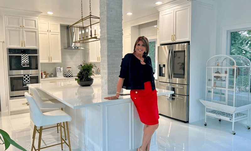 Marcie Manfredonia is wearing a red dress while standing in a white kitchen