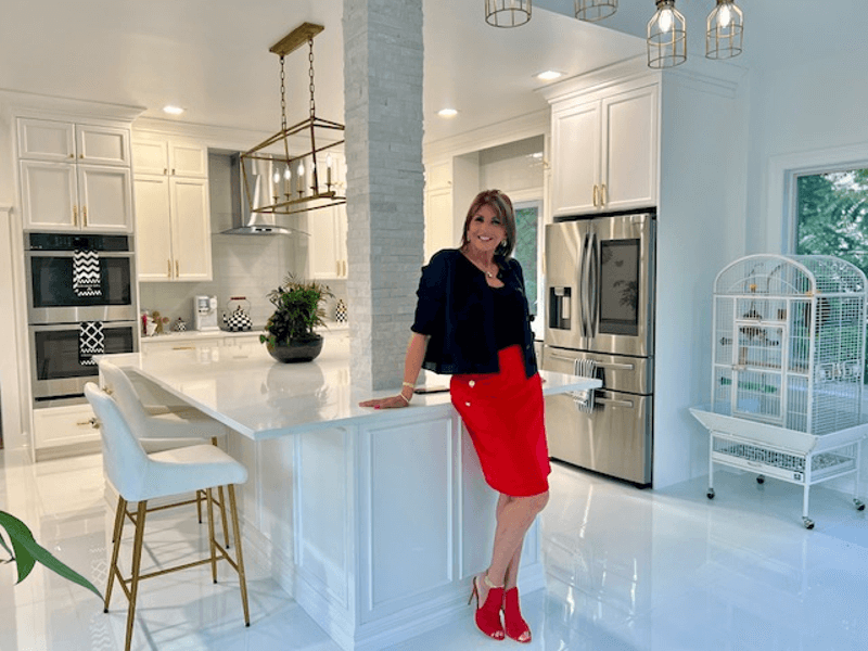 Marcie Manfredonia is wearing a red dress while standing in a white kitchen