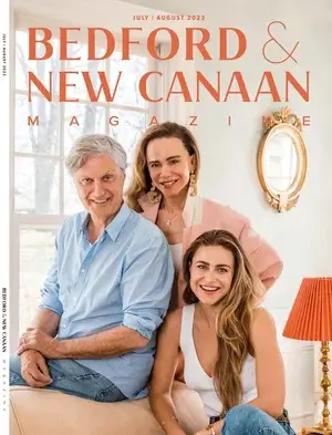 Three smiling adults, two women and one man, pose together indoors in front of a window on the cover of Bedford & New Canaan Magazine, July/August 2023 issue. The setting is bright and warmly decorated.
