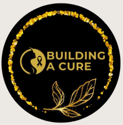 A black circular logo with a gold glitter border, featuring a silhouette of a womans head with a gold ribbon. The text BUILDING A CURE is in gold, with two gold leaves at the bottom.